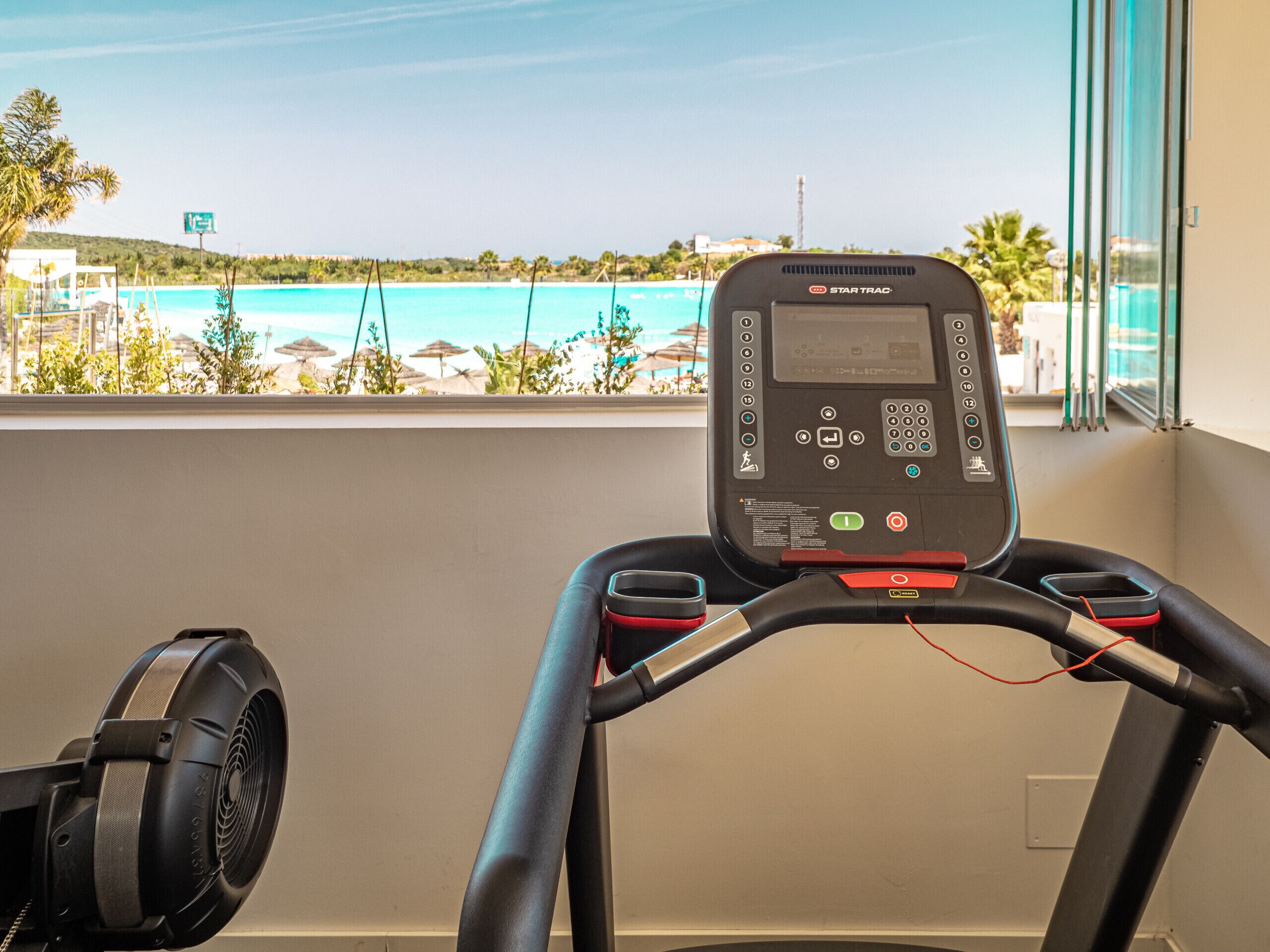 A treadmill with a digital display and control panel, overlooking a beach with umbrellas and palm trees.