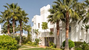 A modern building with white exterior walls, surrounded by lush greenery and palm trees. - Alcazaba Lagoon  2278 Secret Place (Casares)