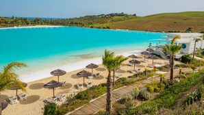 A beach resort with a large turquoise pool, sun loungers, and palm trees. - Alcazaba Lagoon  2278 Secret Place (Casares)