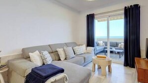 A modern living room with a grey sofa, a small round table, and a view of the sea through large glass doors. - Front Row Penthouse Apartment on Carvajal Beach (Fuengirola)