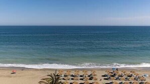 A beach with rows of sun loungers and umbrellas, a clear sky, and the ocean in the background. - Front Row Penthouse Apartment on Carvajal Beach (Fuengirola)