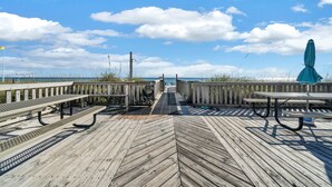 A wooden deck with picnic tables and an umbrella, overlooking a beach with a clear sky. - Okaloosa Island, Beach Service Included, Emerald Isle 206 (Fort Walton Beach)
