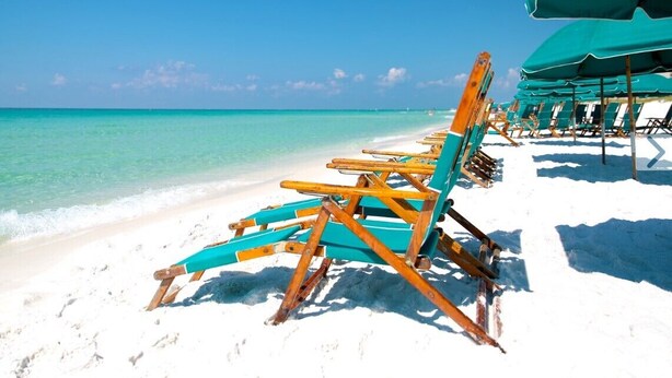 A beach with rows of wooden beach chairs and umbrellas. - Okaloosa Island, Beach Service Included, Emerald Isle 206 (Fort Walton Beach)