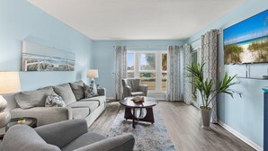 A living room with a grey sofa, a round coffee table, and a potted plant. - Okaloosa Island, Beach Service Included, Emerald Isle 206 (Fort Walton Beach)