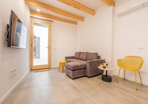 A modern living room with a sectional sofa, a small round table, a yellow chair, and a TV mounted on the wall. - Beautiful Mallorcan house with 2 bedrooms, 1 bathroom, pool and barbecue (Campanet)