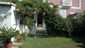 A building with a white exterior, a balcony with white shutters, and a garden area with potted plants and a small tree. - old farmhouse on the sea (Gaeta)