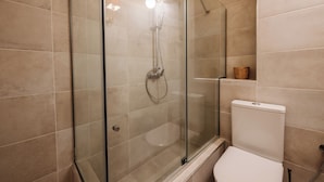 A glass-enclosed shower with a handheld showerhead, a toilet, and a shelf with a basket. - Palaiopolis Maison by Konnect, Mon Repos (Corfu)