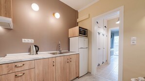 A kitchen with wooden cabinets, a microwave, and a refrigerator. There are two electrical outlets on the wall and a door leading to another room. - Palaiopolis Maison by Konnect, Mon Repos (Corfu)