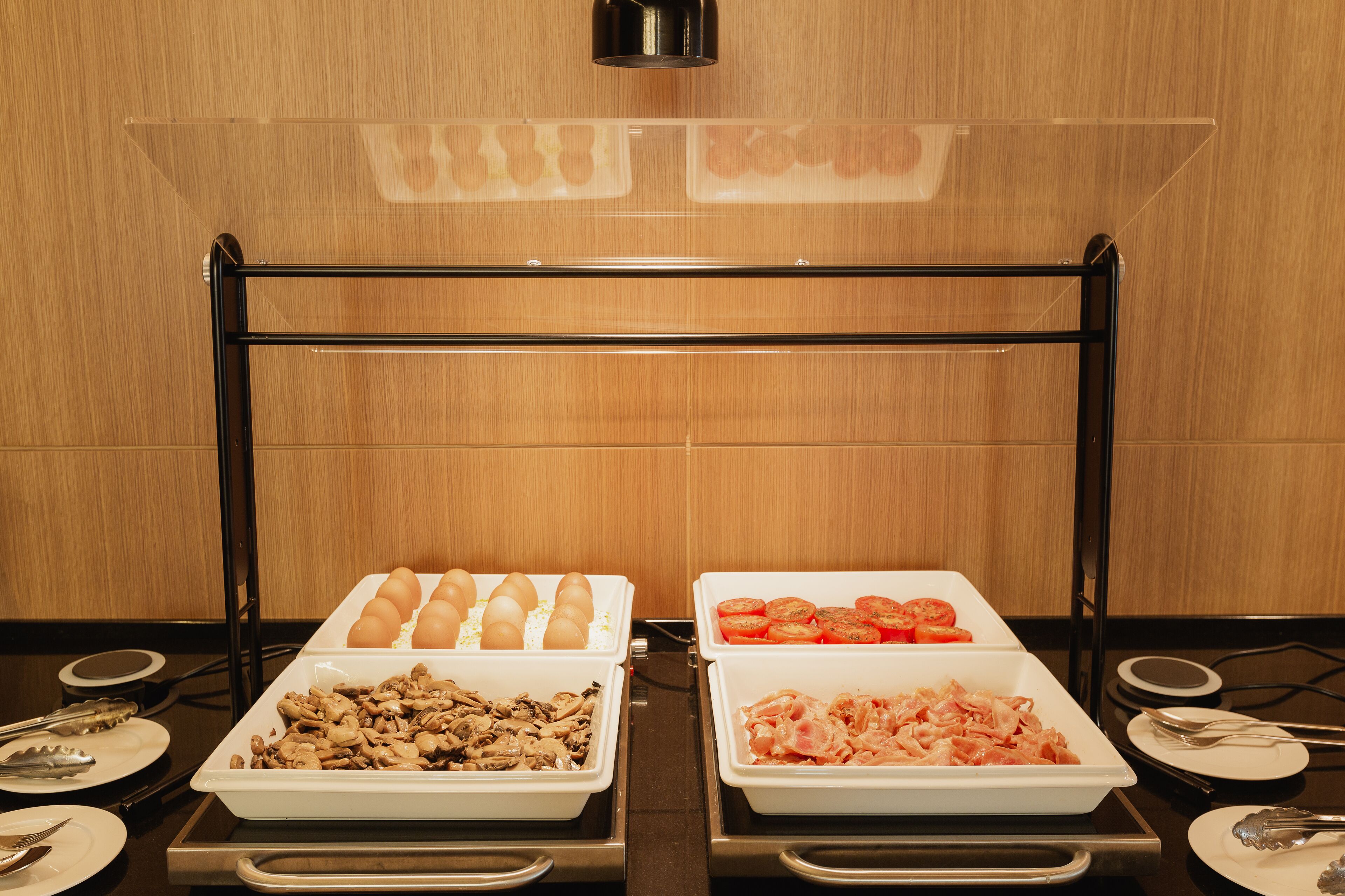 A buffet setup with trays of eggs, mushrooms, tomatoes, and chicken.