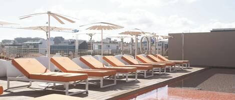 A rooftop pool area with sun loungers and umbrellas.