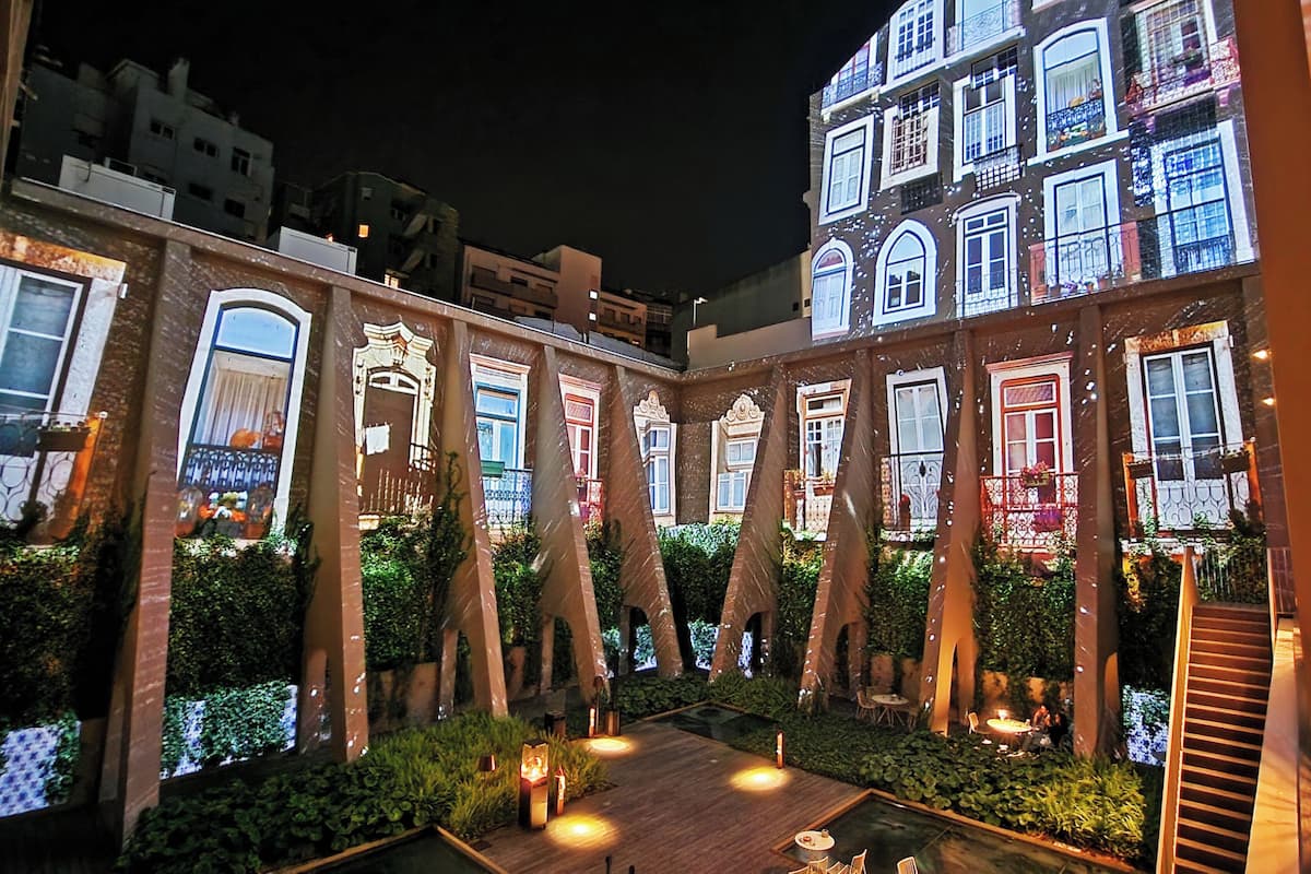 A courtyard with illuminated buildings, a wooden deck, and a small pool.