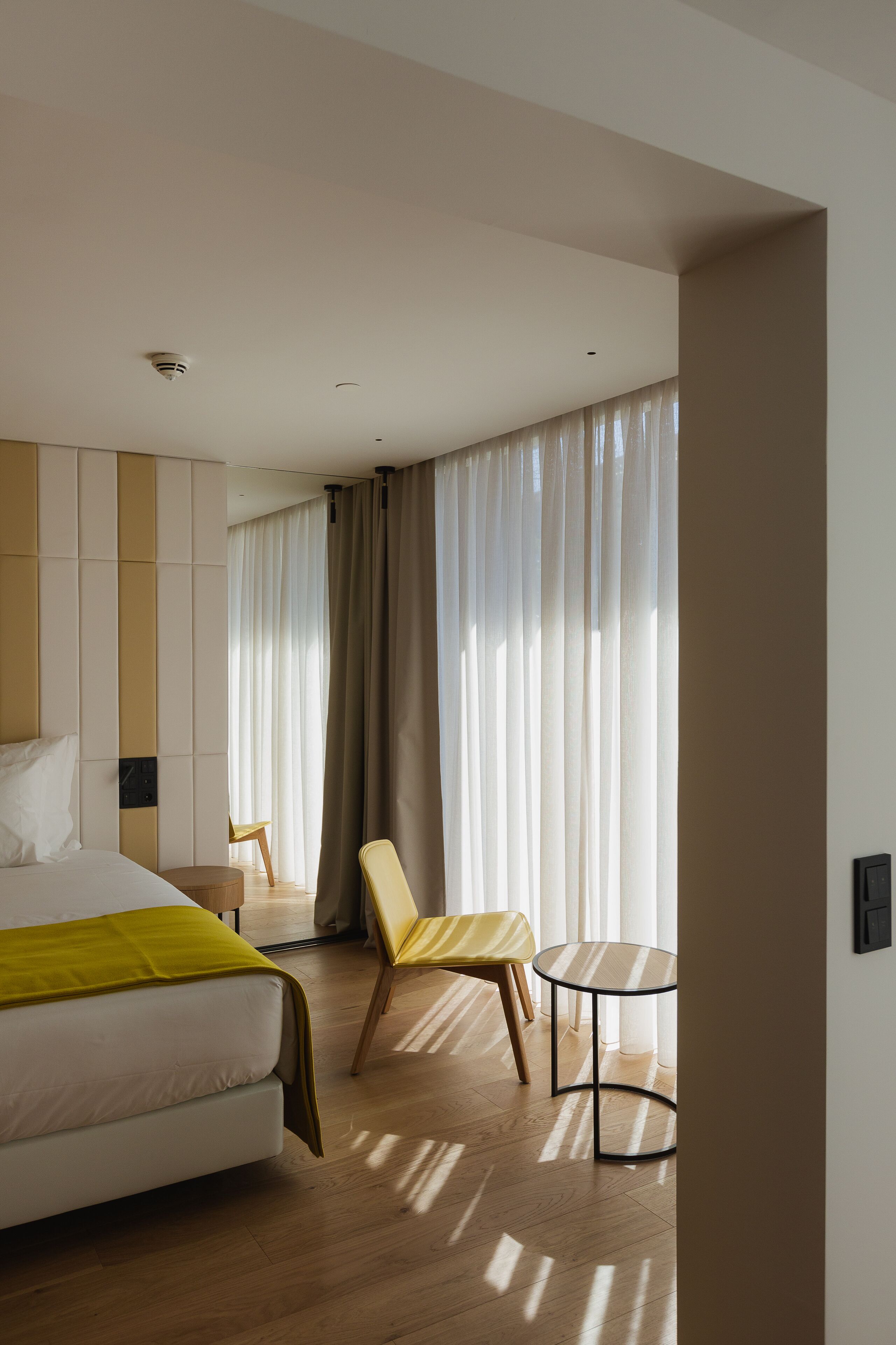 Una habitación de hotel con cama, una silla, una mesita y una ventana con cortinas.