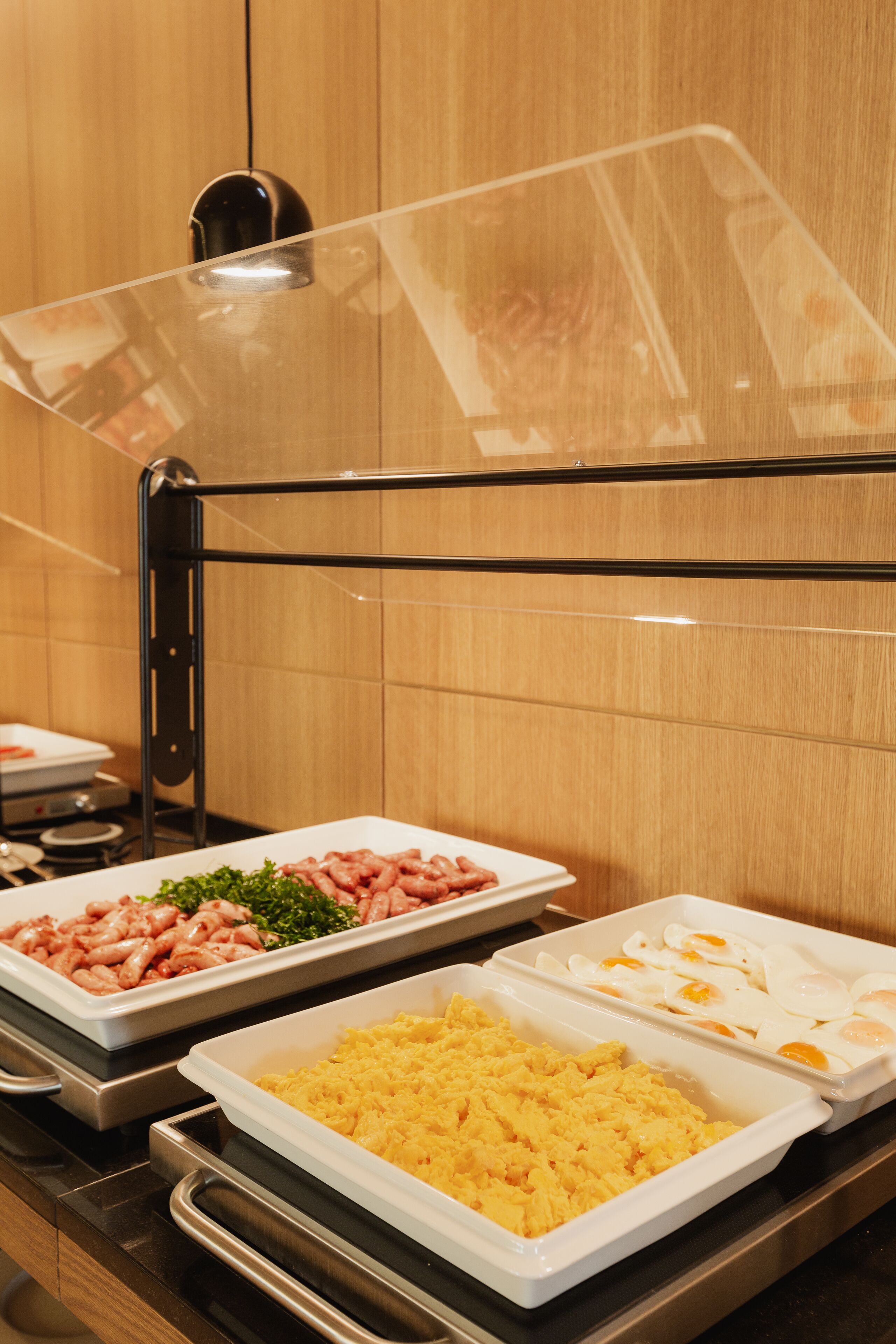Un bufé con diversas opciones de comida, incluyendo huevos revueltos, salchichas y una ensalada.