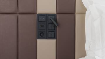 A modern room with a padded wall, a control panel, a wooden side table, and a white bed.