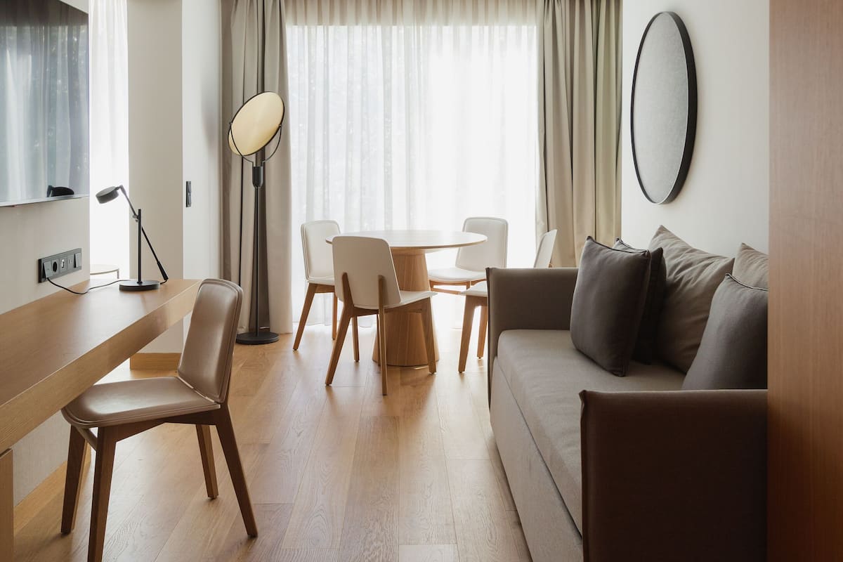 A modern living room with a wooden floor, a sofa, a coffee table, and a dining area with chairs and a lamp.