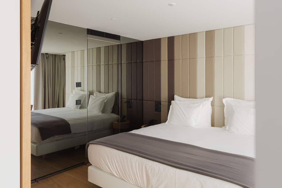 A modern hotel room with a large bed, a bedside table, a mirror, and a wall with vertical paneling.
