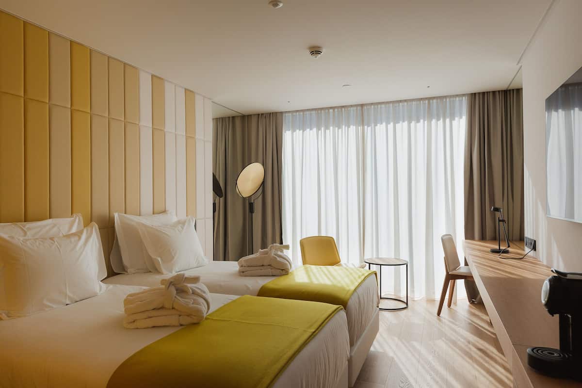 A hotel room with two beds, a small table, a chair, and a desk with a lamp.