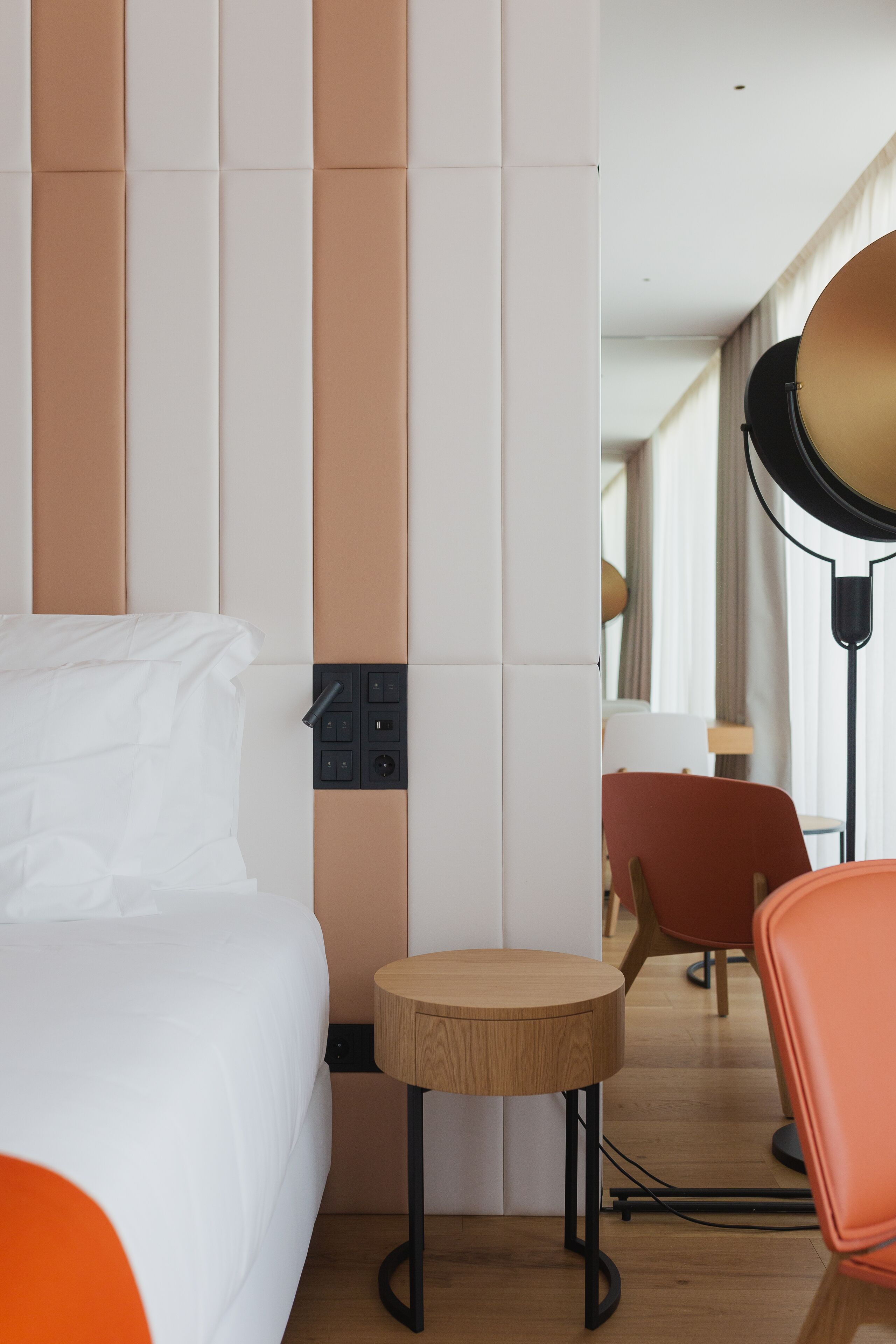 A hotel room with a bed, a small wooden table, a chair, and a lamp.