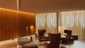 A modern lounge area with a wooden panel wall, a large window with vertical blinds, and contemporary furniture including chairs and ottomans. - Lumen Hotel & The Lisbon Light Show (Lisbon)