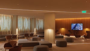 A modern lounge area with sofas, ottomans, and chairs, a flat-screen TV displaying an aerial view, and a wooden accent wall.