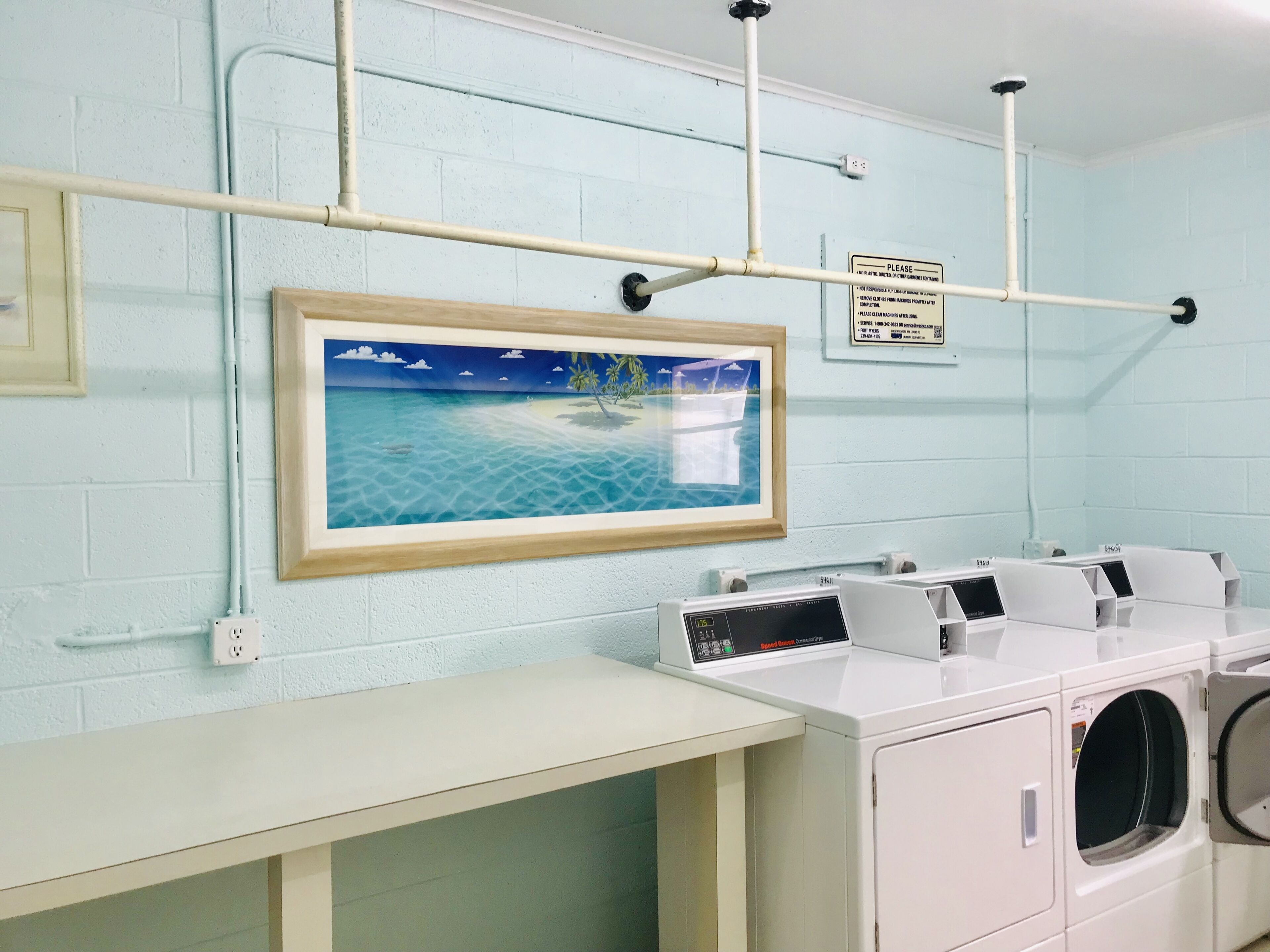 A laundry area with a wall-mounted washing machine, a drying rack, and a framed picture of a beach scene.