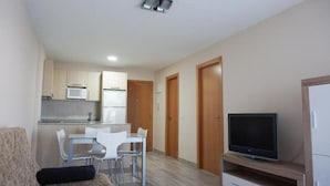Ett kompakt bostadsutrymme med ett litet kök, en matplats, en soffa och en tv.