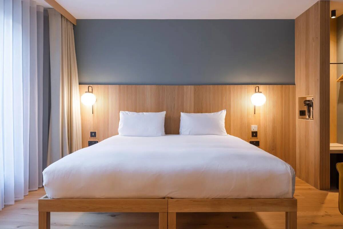 A double bed with a wooden headboard, two bedside lamps, and a wooden floor.