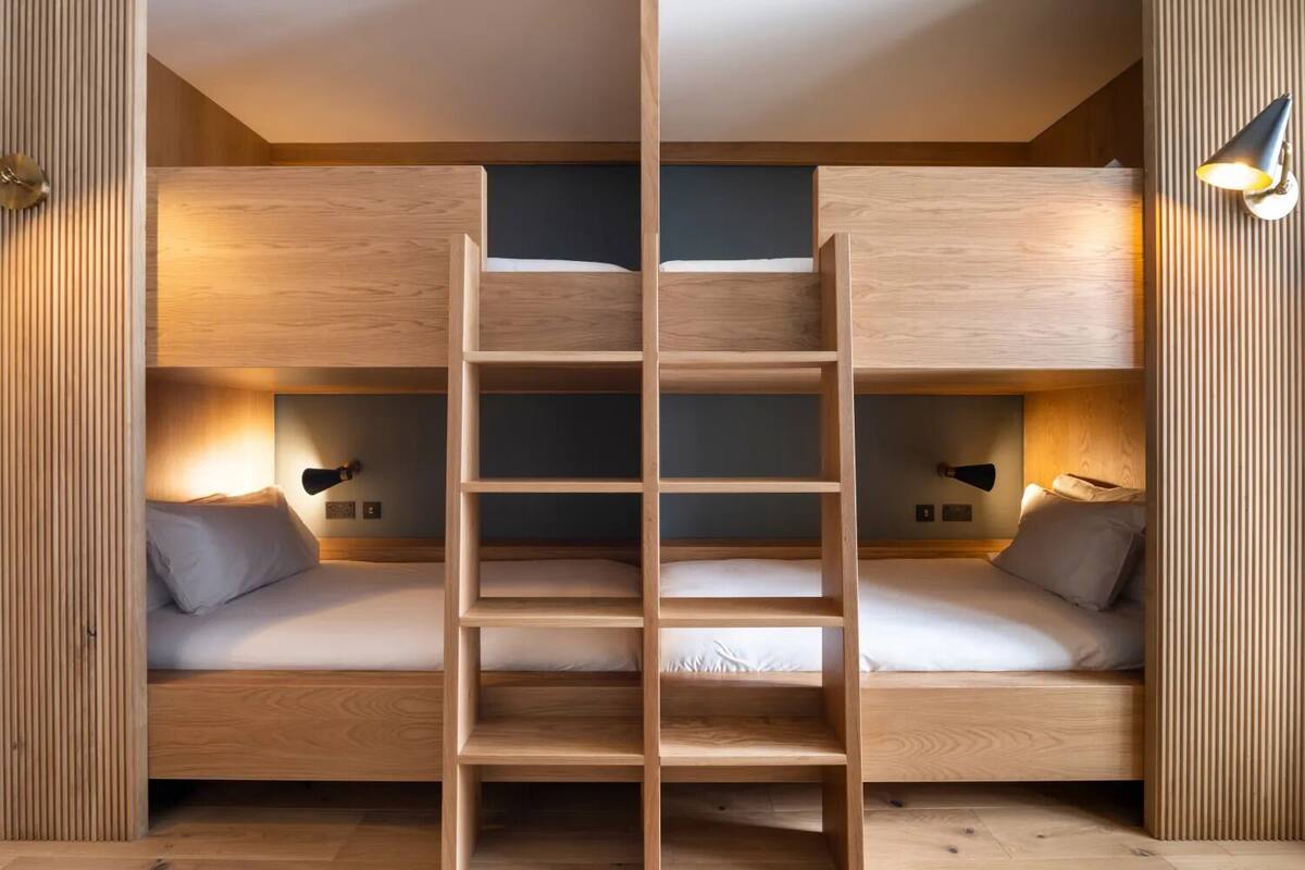 A bunk bed room with a central ladder, wooden walls, and bedside lamps.