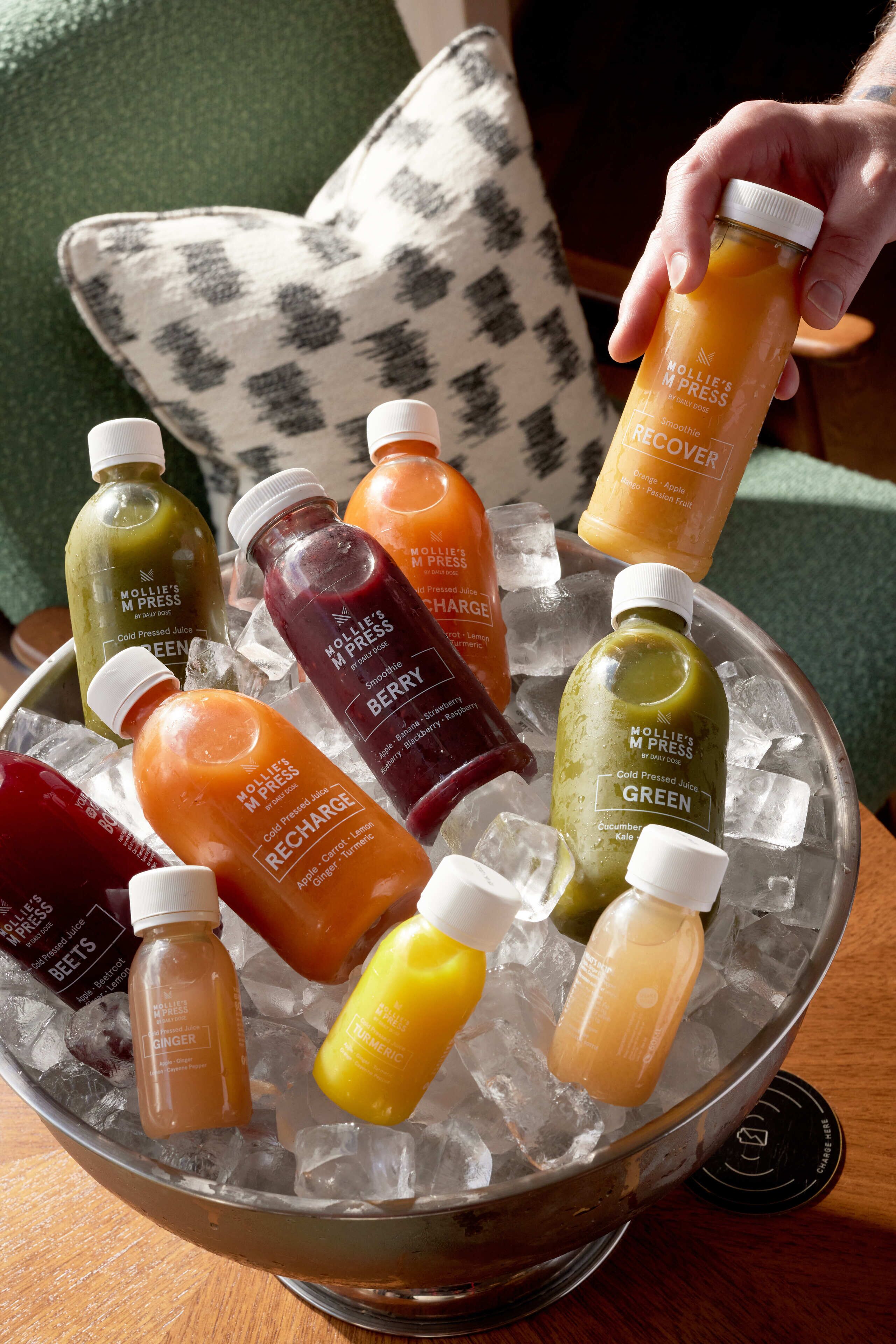 A variety of cold-pressed juices in a metal container with ice cubes.
