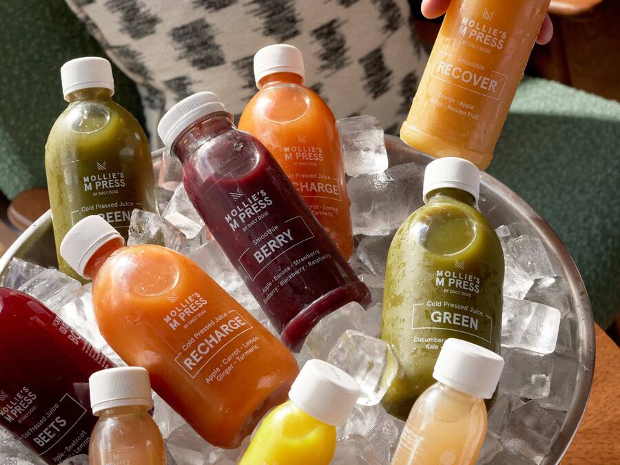 A variety of cold-pressed juices in a metal container with ice cubes.