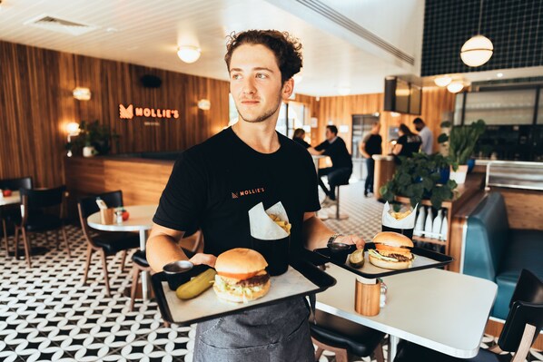 A person serving food at a restaurant with a wooden interior and a checkered floor pattern.