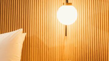 A hotel room with a bed, a bedside table, a wall-mounted light fixture, and a control panel.