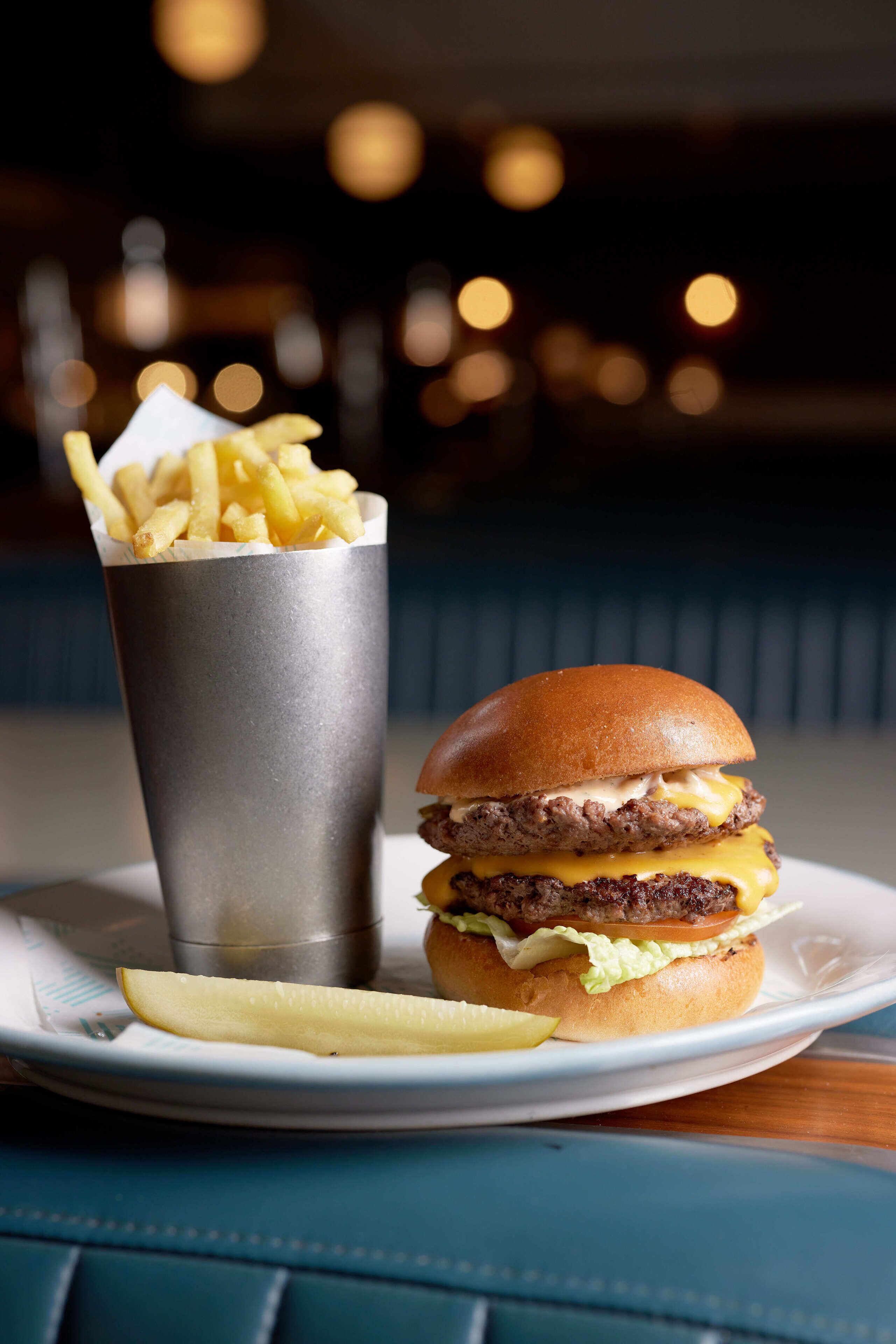 A burger with fries on a plate, a drink in a metal cup, and a table with a blue surface.