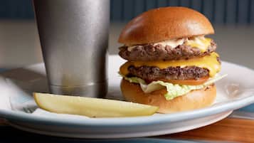 A burger with fries on a plate, a drink in a metal cup, and a table with a blue surface.
