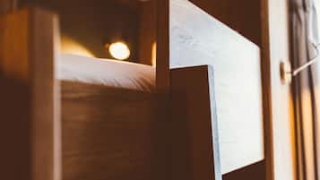 Una cama litera de madera con cabecera, una lámpara de noche y una ventana con cortinas.