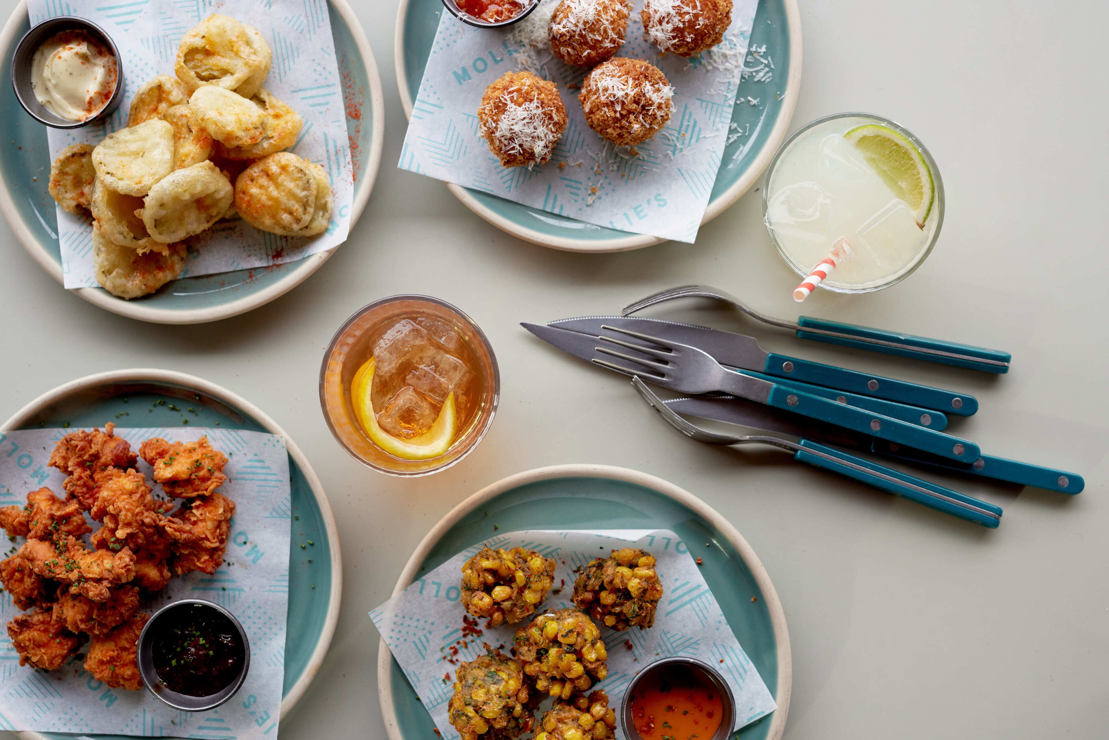 A table with various fried foods and drinks, including a glass with a lime slice and a cup of sauce.
