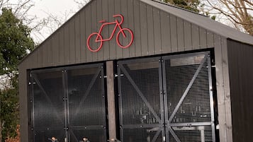 Un edificio con un símbolo de bicicleta sobre la entrada, dos bicicletas con cestas estacionadas al frente y un área techada.