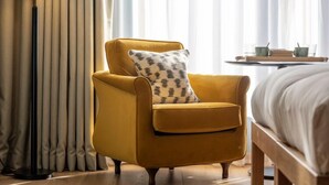 Una camera d'albergo con una poltrona gialla, un comodino con una lampada e un letto.