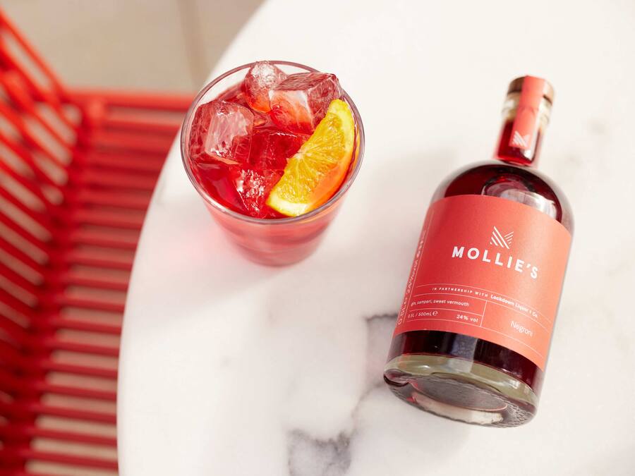 Un vaso de bebida roja con hielo y una rodaja de naranja, y una botella de licor con etiqueta roja.