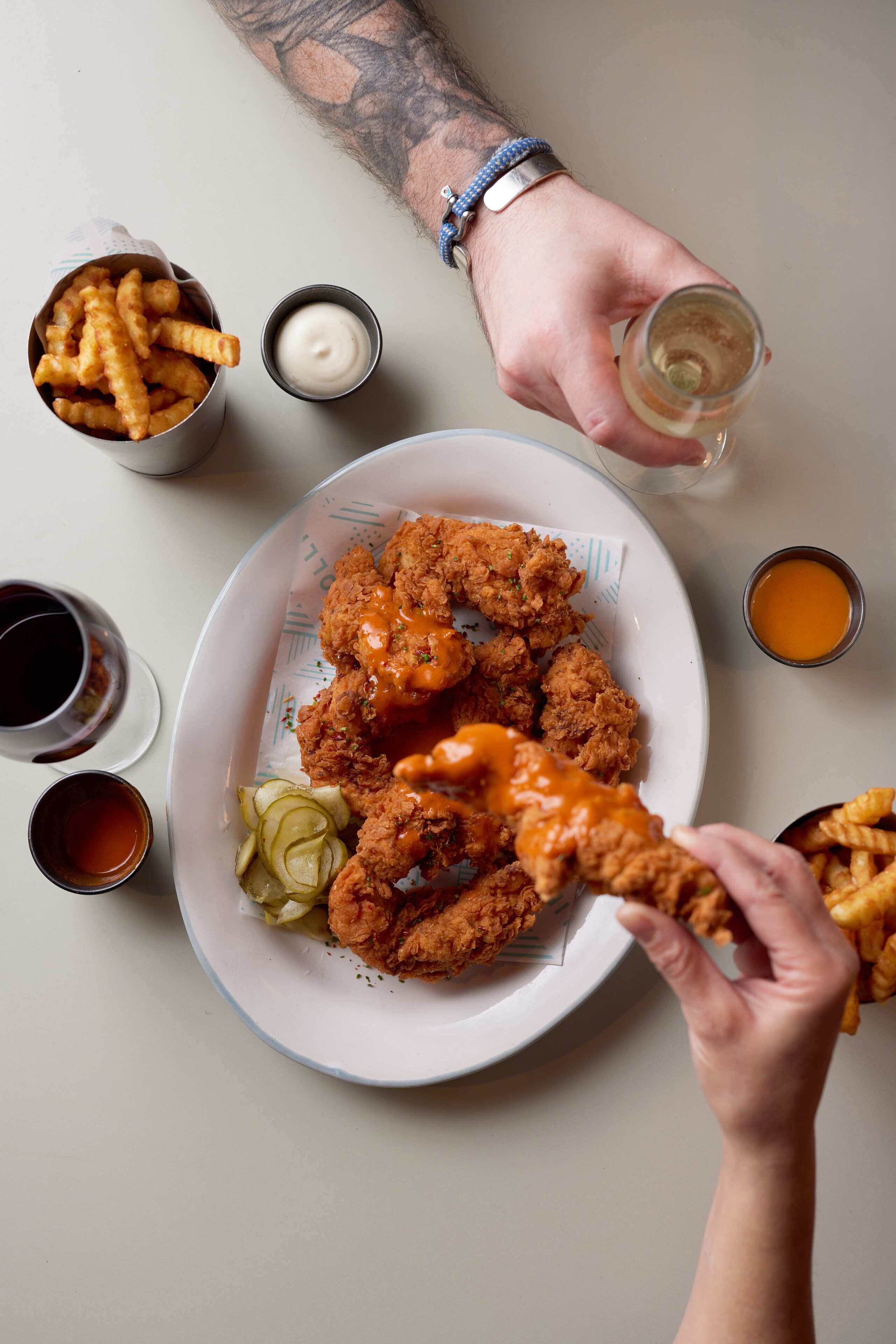 A plate of fried chicken and fries with dipping sauces, a glass of white wine, and a cup of coffee on a table.