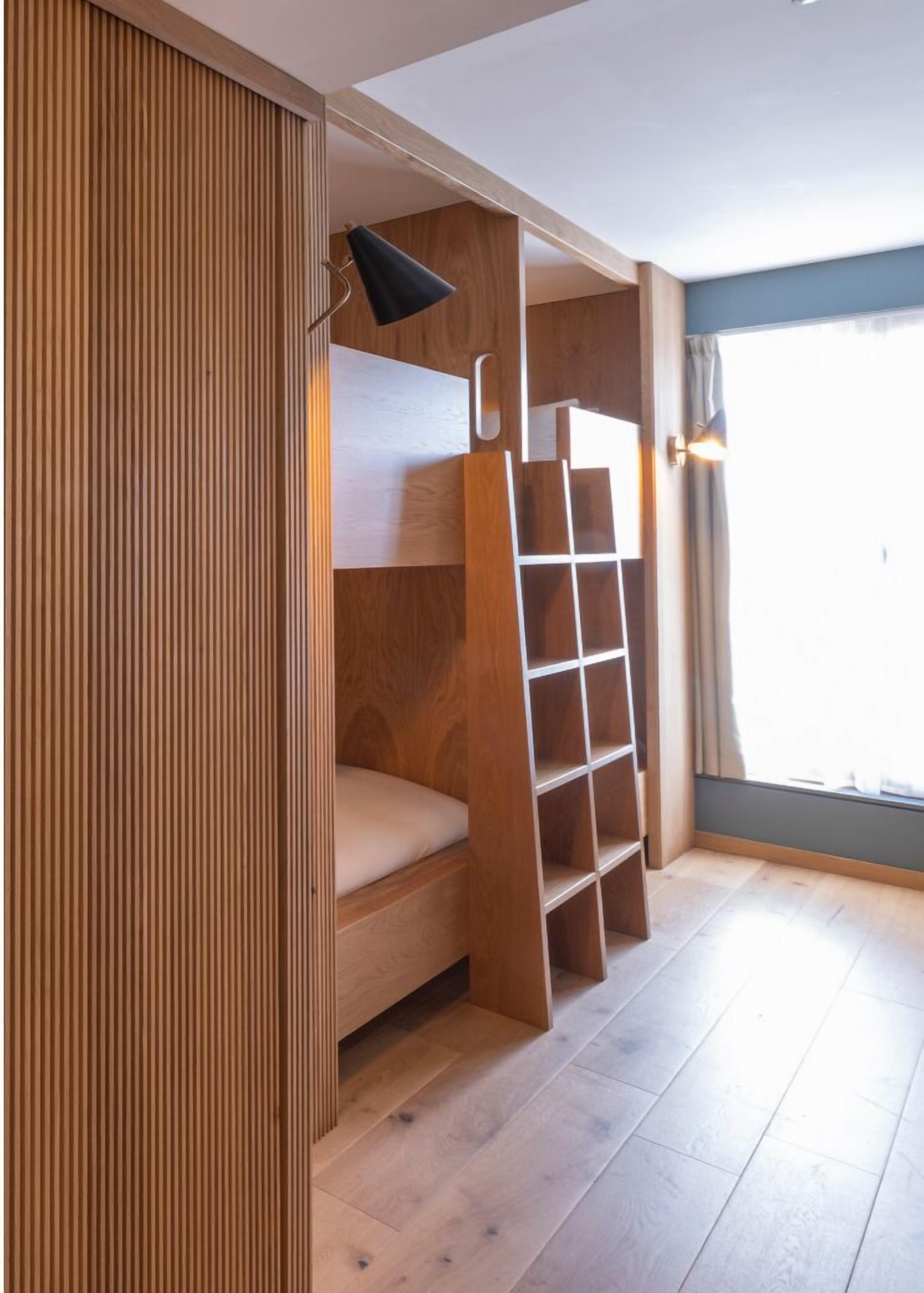 Habitación con literas, un panel de pared de madera, un escritorio pequeño con lámpara y una ventana con cortinas.