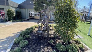 Eine angelegte Gartenanlage mit einer Metallskulptur, geschnittenen Büschen und einem großen Baum.