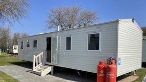 Ein Wohnmobil mit Haustür, einer kleinen Veranda und einem Fenster. Zwei Propangasflaschen stehen draußen.