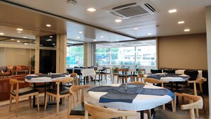 A restaurant with round tables, chairs, and a seating area with sofas. - Kanak Beacon Hotel  (Ahmedabad)