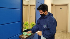 A person cleaning a mirror in a hotel room with blue walls and wooden floors. - Kanak Beacon Hotel  (Ahmedabad)