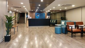 A modern reception area with a reception desk, seating area, and a staircase leading to upper floors. - Kanak Beacon Hotel  (Ahmedabad)