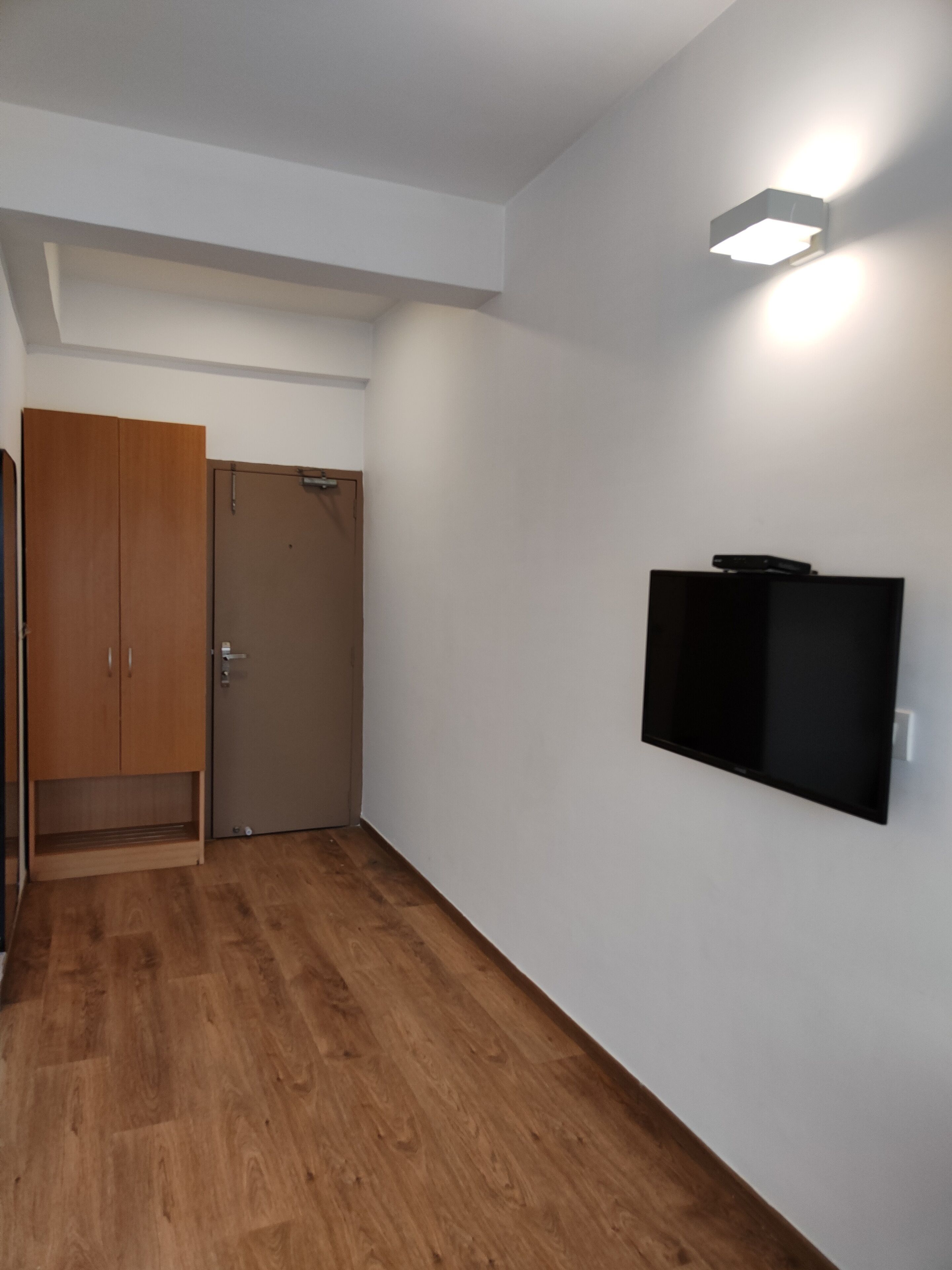 Une pièce avec une armoire en bois, une porte fermée, un téléviseur à écran plat fixé au mur et un luminaire sur le mur.