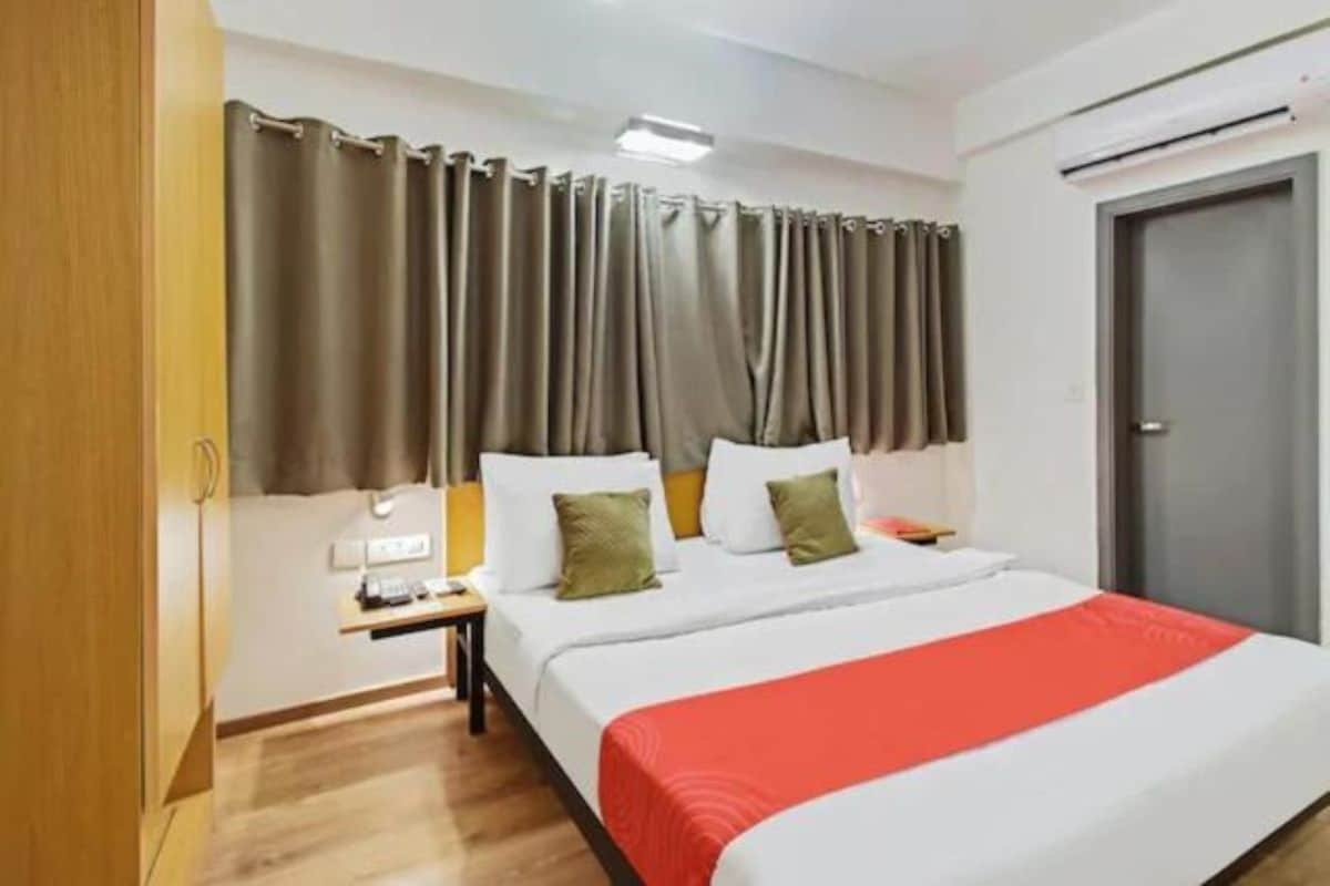 Ein Hotelzimmer mit Bett, Vorhängen, Nachttisch, Lampe und einer Tür.