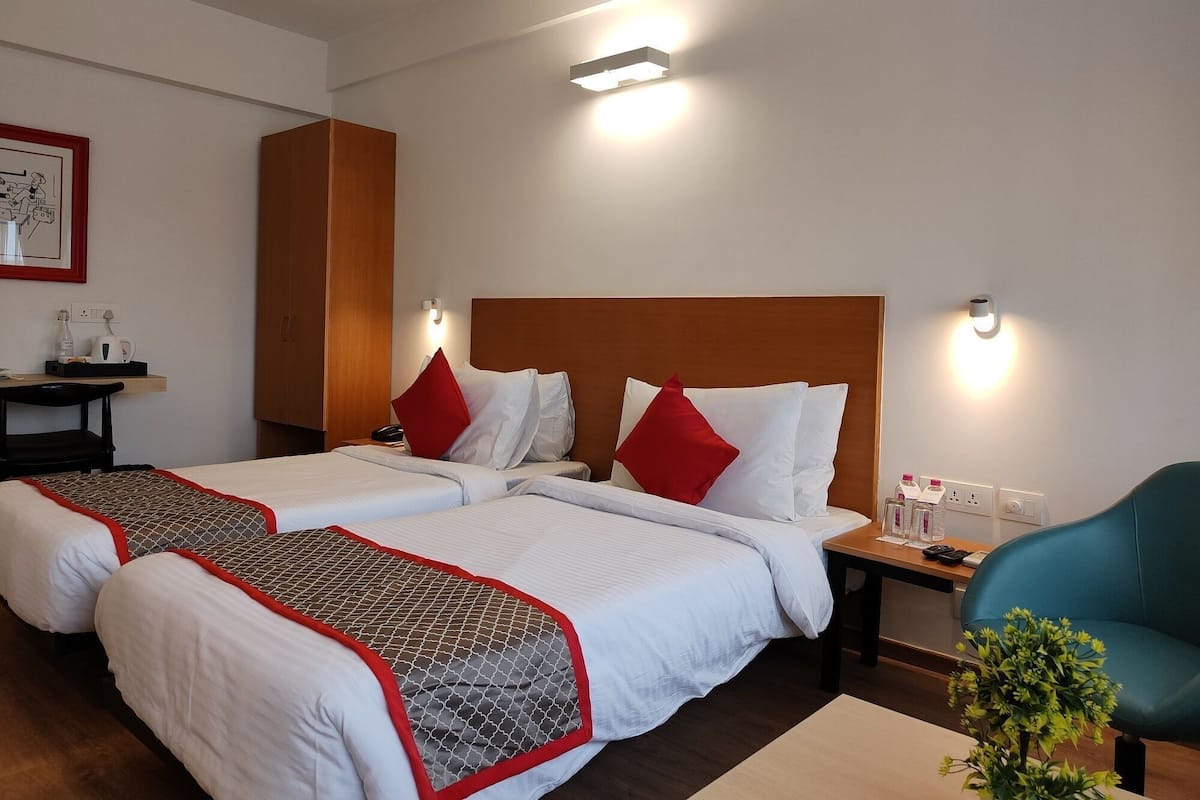 Ett hotellrum med två sängar, ett skrivbord, en stol och ett litet bord med diverse bekvämligheter.