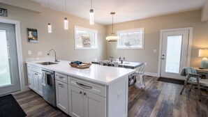 Une cuisine moderne avec des meubles blancs, un grand îlot central et des luminaires suspendus.